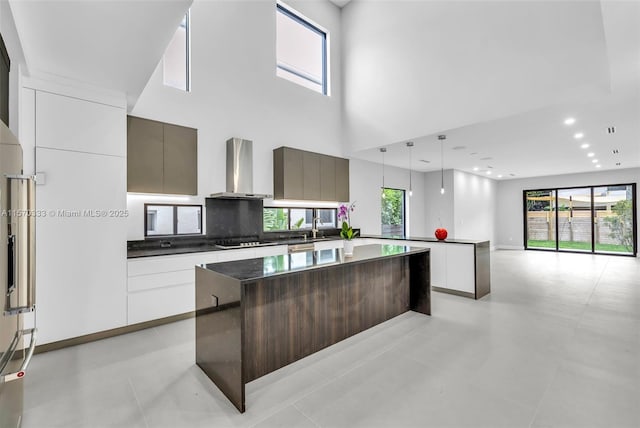 kitchen with wall chimney exhaust hood, sink, black cooktop, a kitchen island, and pendant lighting