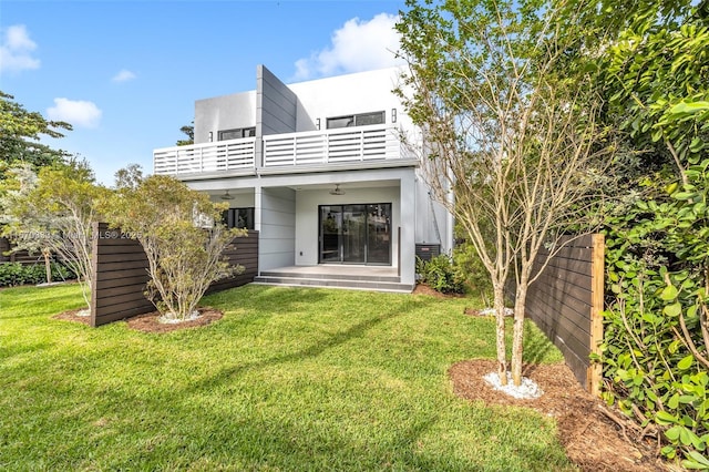 rear view of property featuring a balcony, a yard, and ceiling fan