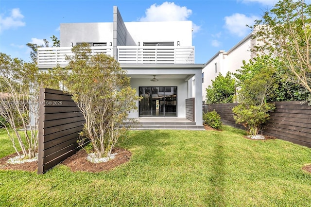 rear view of property with ceiling fan, a lawn, and a balcony