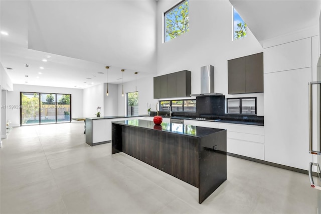 kitchen featuring dark brown cabinetry, wall chimney exhaust hood, white cabinetry, hanging light fixtures, and a kitchen island