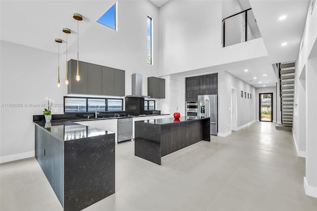 kitchen featuring wall chimney exhaust hood, sink, a center island, appliances with stainless steel finishes, and pendant lighting