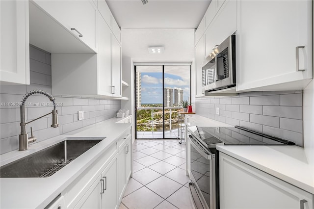 kitchen with light tile patterned floors, sink, white cabinets, floor to ceiling windows, and stainless steel appliances