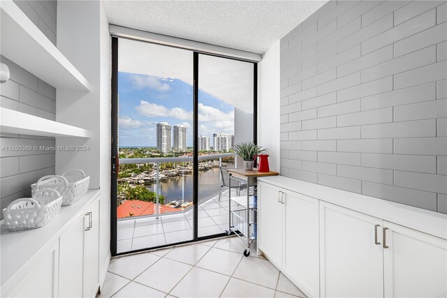 doorway with a textured ceiling, light tile patterned floors, expansive windows, and a water view