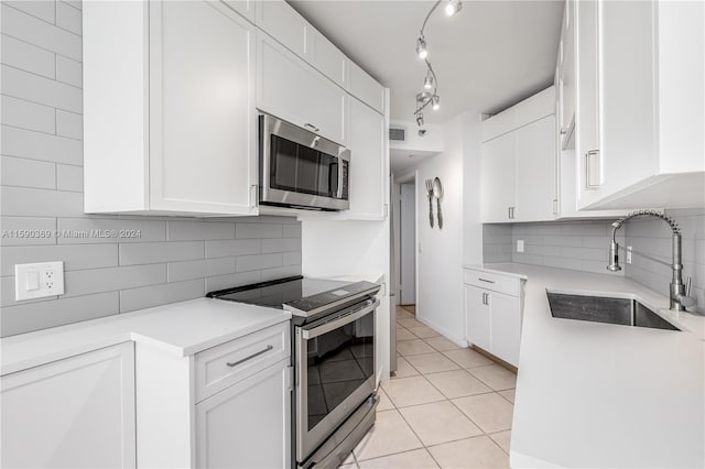 kitchen with appliances with stainless steel finishes, sink, backsplash, white cabinetry, and light tile patterned floors