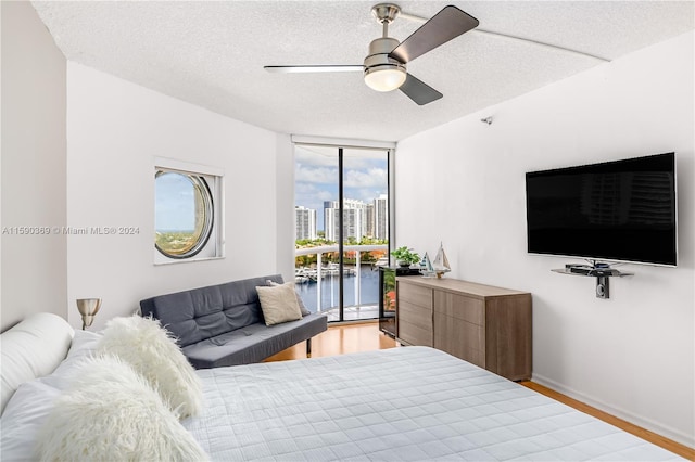 bedroom featuring ceiling fan, light hardwood / wood-style floors, a textured ceiling, and a wall of windows