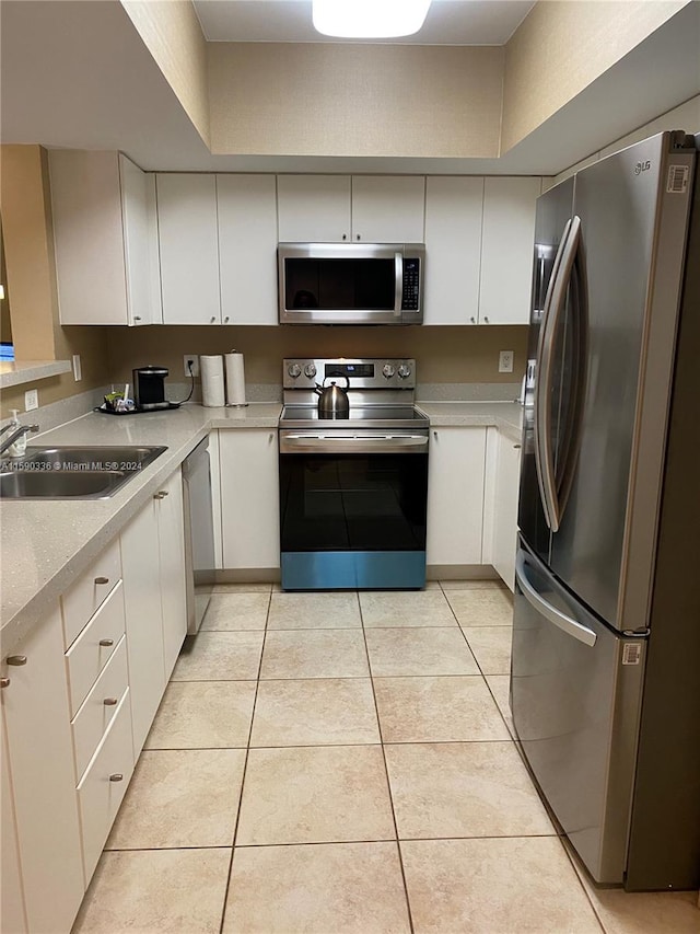 kitchen with appliances with stainless steel finishes, white cabinetry, sink, and light tile flooring