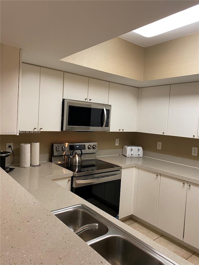 kitchen with appliances with stainless steel finishes, white cabinetry, light stone countertops, and sink