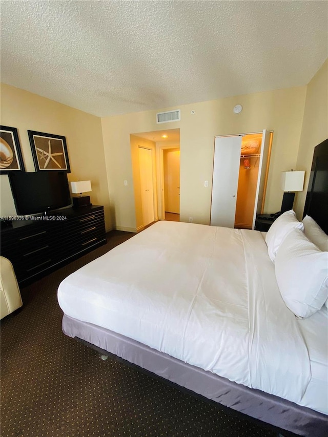 bedroom featuring a closet, a textured ceiling, dark carpet, and a spacious closet