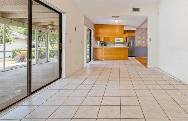 kitchen featuring a healthy amount of sunlight, tasteful backsplash, stainless steel refrigerator with ice dispenser, and light tile floors