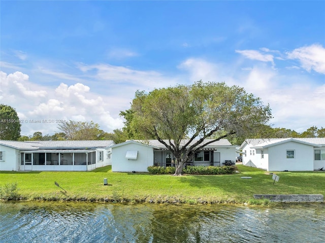 back of house with a sunroom, a water view, and a yard