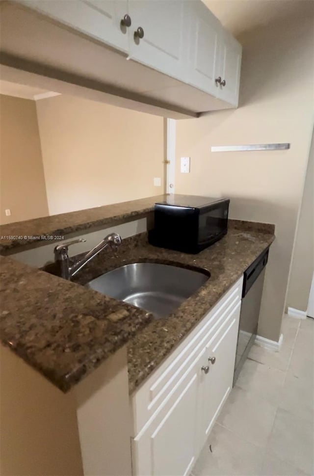 kitchen featuring white cabinetry, stainless steel dishwasher, dark stone countertops, sink, and light tile floors