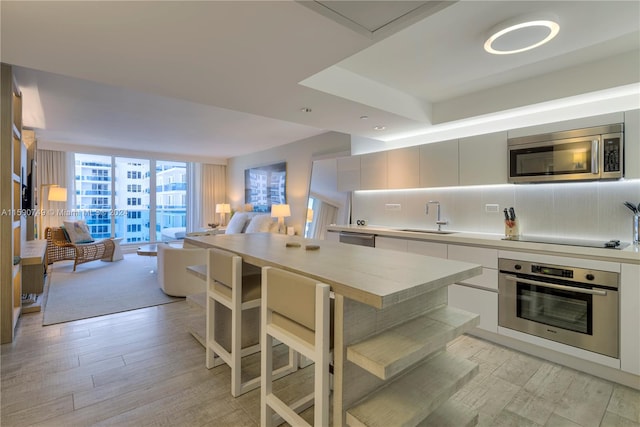 kitchen with light wood-type flooring, stainless steel appliances, backsplash, floor to ceiling windows, and sink