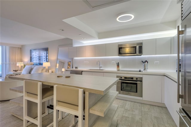 kitchen with light hardwood / wood-style floors, appliances with stainless steel finishes, backsplash, sink, and a kitchen bar