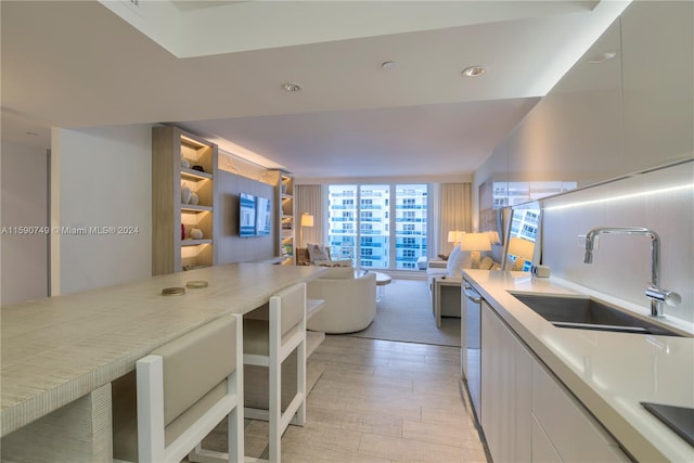 kitchen featuring light hardwood / wood-style floors, white cabinets, backsplash, a wall of windows, and sink