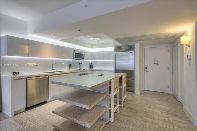 kitchen with appliances with stainless steel finishes, sink, tasteful backsplash, and light wood-type flooring