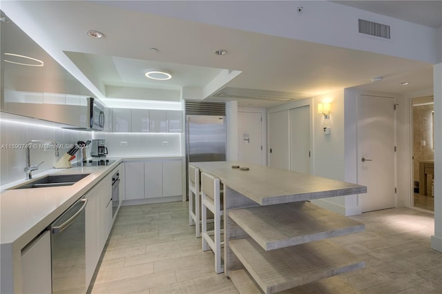 kitchen featuring tasteful backsplash, sink, white cabinets, a breakfast bar area, and appliances with stainless steel finishes