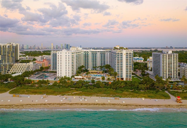 aerial view at dusk featuring a view of the beach and a water view