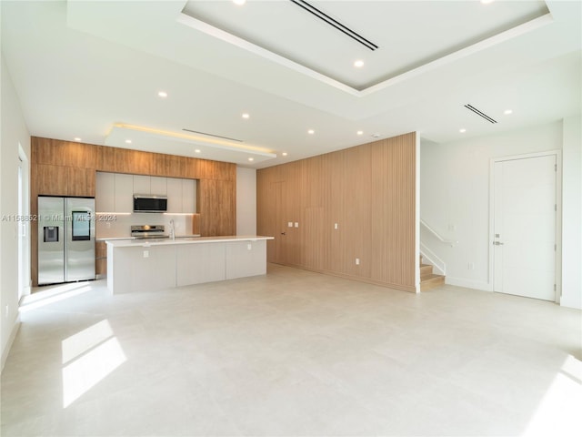 kitchen with a large island, appliances with stainless steel finishes, wood walls, and a tray ceiling