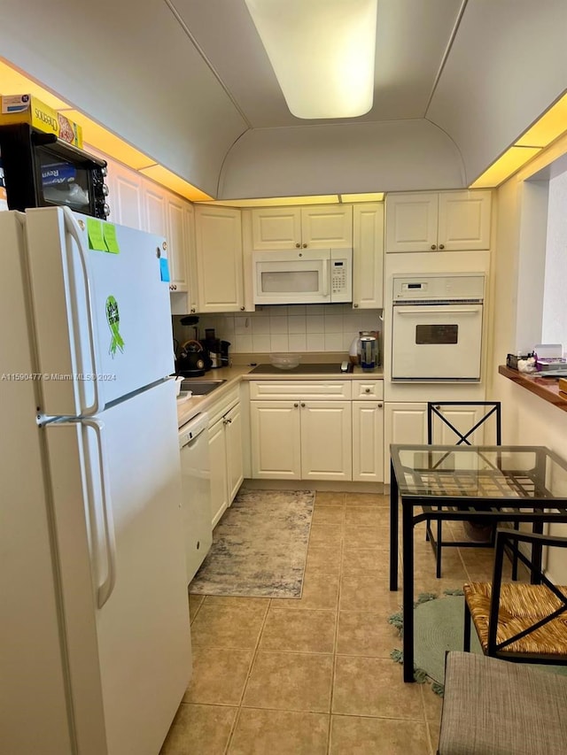 kitchen with white appliances, backsplash, light tile floors, sink, and white cabinets