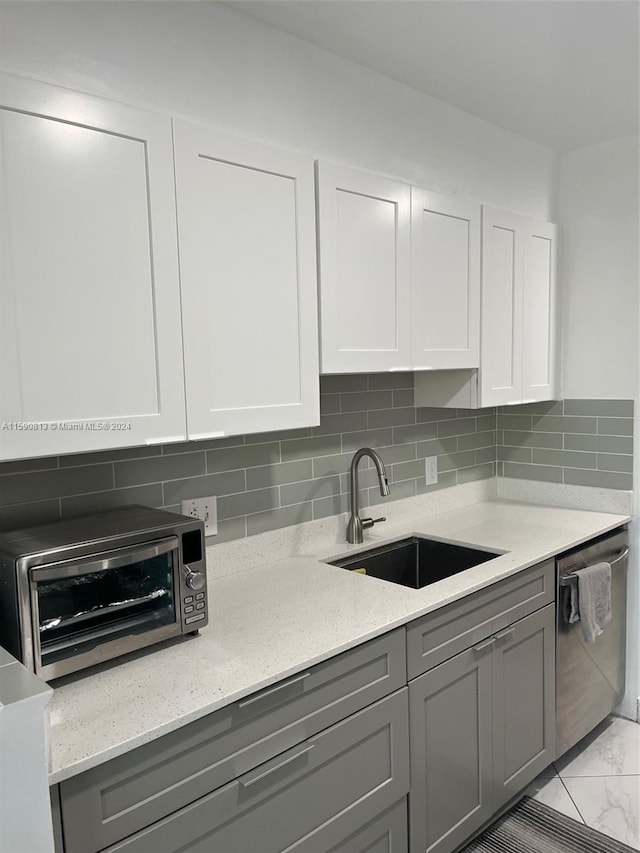 kitchen with tasteful backsplash, sink, stainless steel dishwasher, and gray cabinets