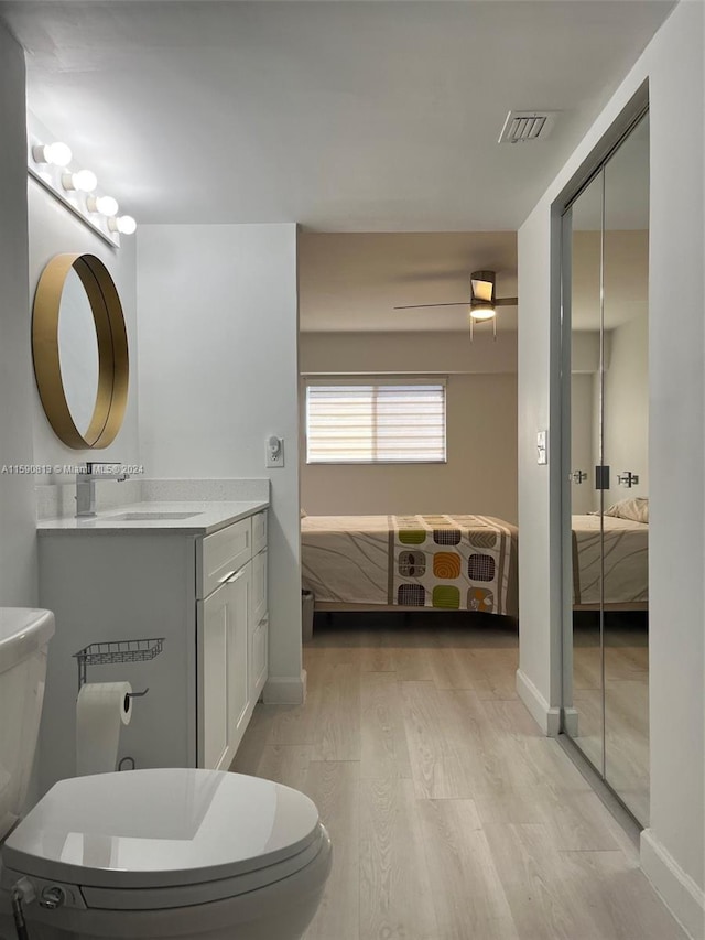 bathroom with hardwood / wood-style floors, ceiling fan, toilet, and vanity with extensive cabinet space