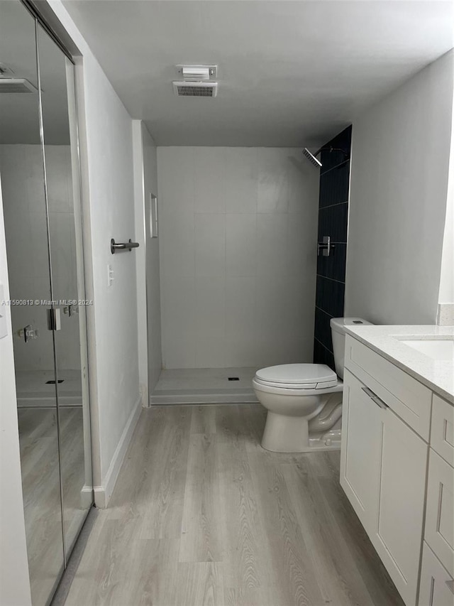 bathroom with tiled shower, wood-type flooring, toilet, and vanity