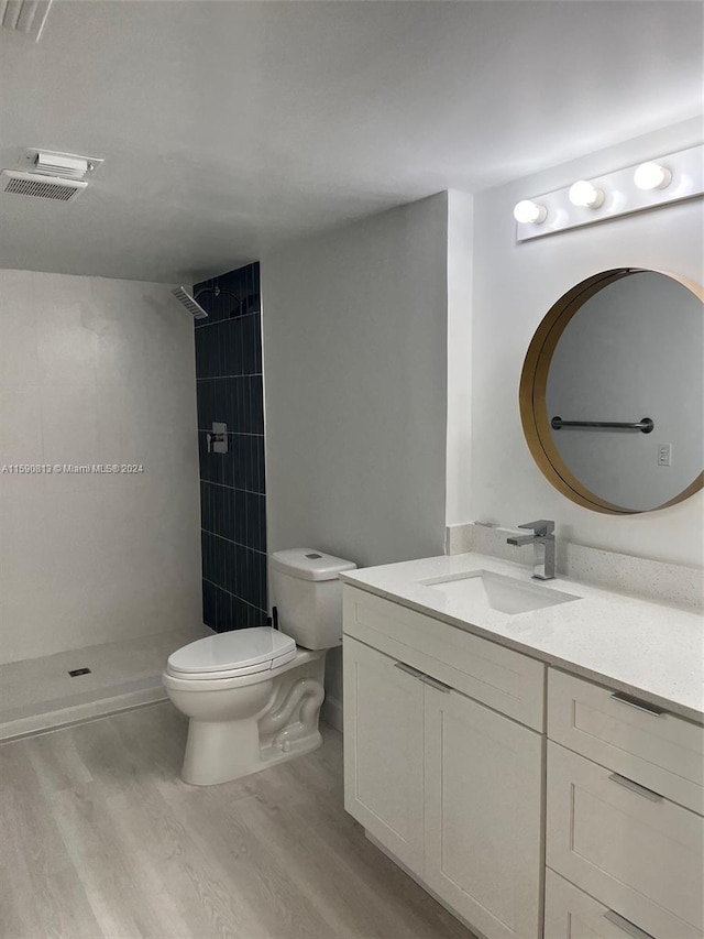 bathroom with a tile shower, wood-type flooring, oversized vanity, and toilet