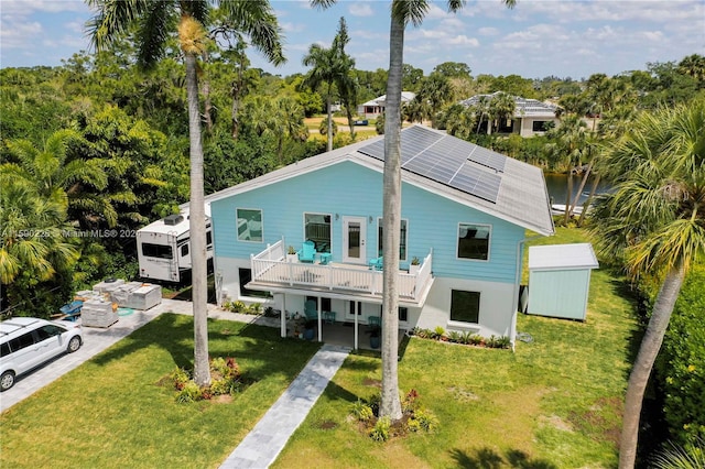 rear view of property featuring a balcony, solar panels, a shed, and a lawn