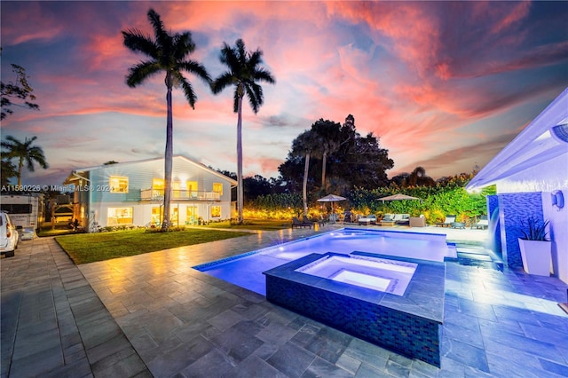 pool at dusk with a patio, pool water feature, a lawn, and an in ground hot tub