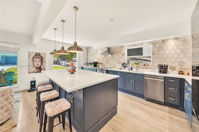 kitchen featuring stainless steel appliances, decorative light fixtures, backsplash, a center island, and wall chimney exhaust hood