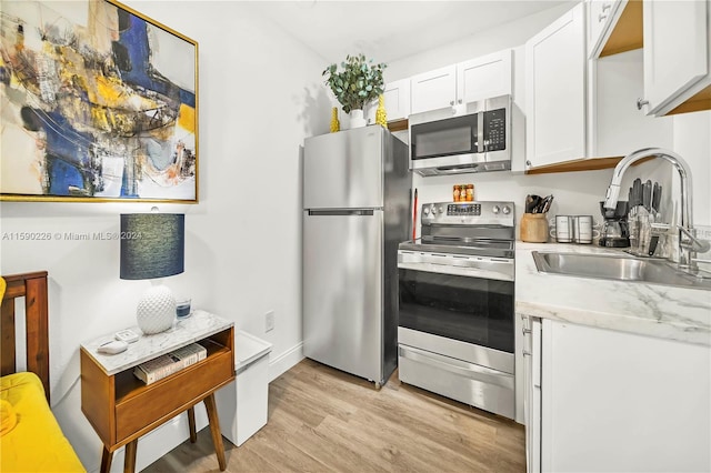 kitchen with light stone counters, light hardwood / wood-style floors, white cabinets, sink, and appliances with stainless steel finishes