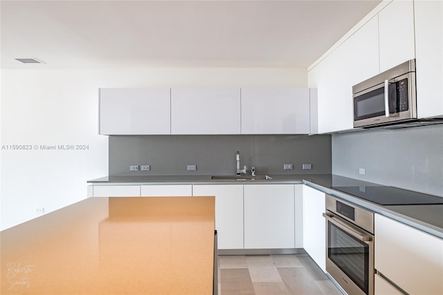 kitchen with white cabinetry, light hardwood / wood-style flooring, appliances with stainless steel finishes, backsplash, and sink