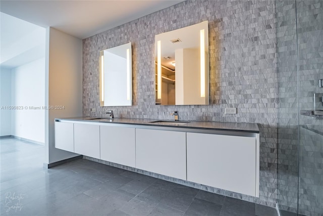 bathroom featuring backsplash, tile floors, large vanity, walk in shower, and double sink