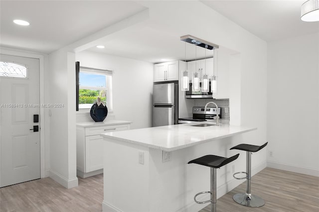 kitchen with hanging light fixtures, stainless steel appliances, light hardwood / wood-style floors, and white cabinets