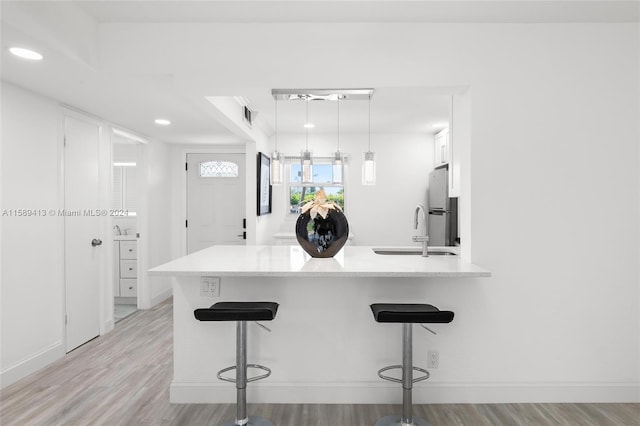 kitchen with sink, light hardwood / wood-style floors, a breakfast bar, and kitchen peninsula