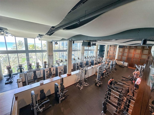 workout area with tile floors, a water view, and a wall of windows