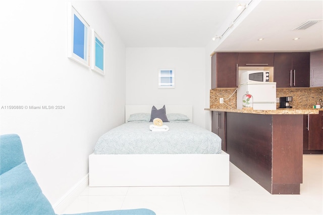 bedroom featuring light tile flooring, track lighting, and white refrigerator