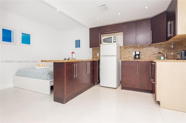 kitchen with dark brown cabinets, tasteful backsplash, white appliances, light stone counters, and light tile floors