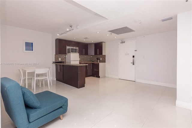 kitchen with dark brown cabinets, tasteful backsplash, white fridge, stainless steel microwave, and light tile floors