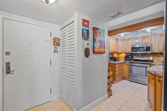 kitchen featuring stainless steel appliances, light tile floors, light stone counters, and backsplash