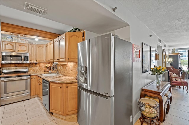 kitchen with appliances with stainless steel finishes, light stone counters, sink, tasteful backsplash, and light tile floors