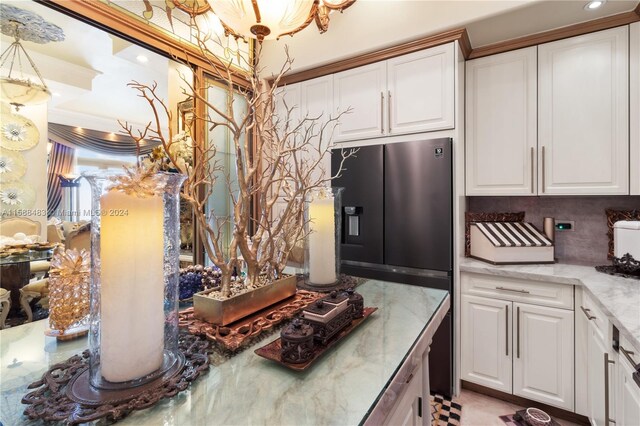 kitchen with light stone counters, stainless steel fridge with ice dispenser, tasteful backsplash, white cabinetry, and ornamental molding