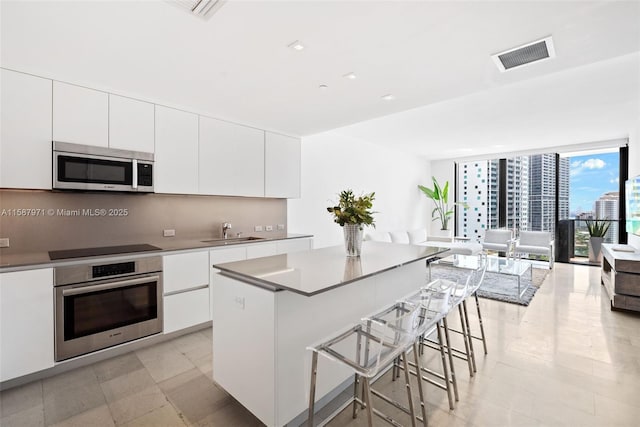 kitchen featuring stainless steel appliances, sink, white cabinets, a breakfast bar area, and a kitchen island