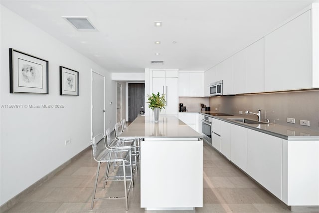 kitchen with a center island, a kitchen bar, white cabinets, appliances with stainless steel finishes, and sink