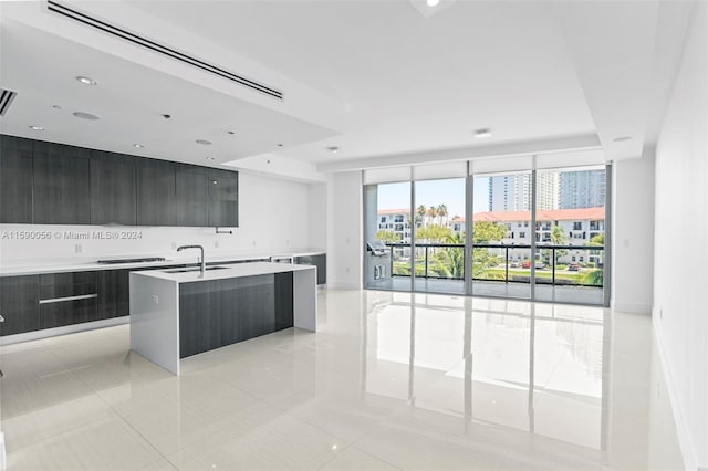 kitchen featuring sink, a wall of windows, light tile floors, and a kitchen island with sink