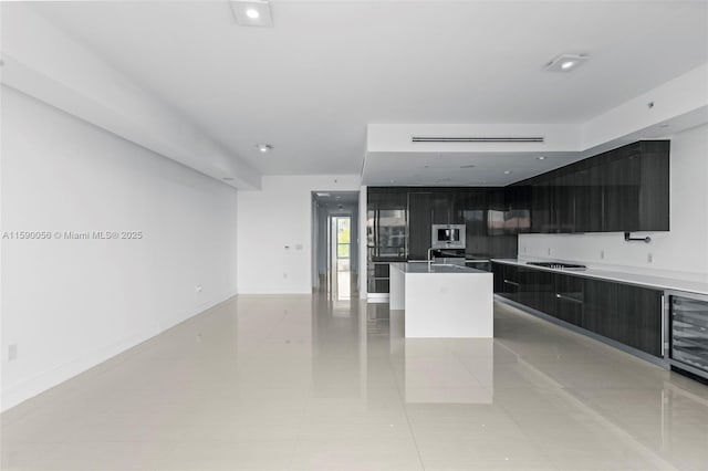 kitchen with modern cabinets, light tile patterned floors, a center island with sink, appliances with stainless steel finishes, and beverage cooler