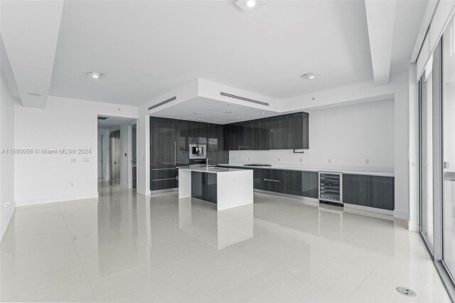 kitchen featuring beverage cooler, a center island with sink, built in microwave, light tile flooring, and sink