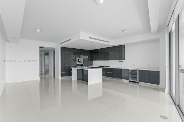 kitchen with beverage cooler, stainless steel microwave, light countertops, modern cabinets, and a center island with sink