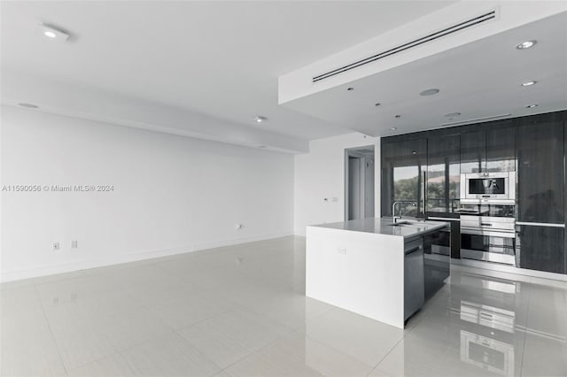 kitchen with an island with sink, sink, light tile floors, and stainless steel appliances