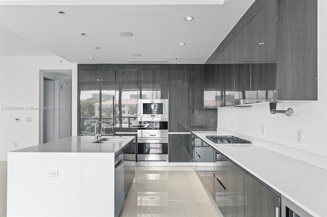 kitchen featuring an island with sink, sink, light tile flooring, and stainless steel appliances